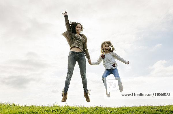 Happy mother and daughter jumping on a meadow
