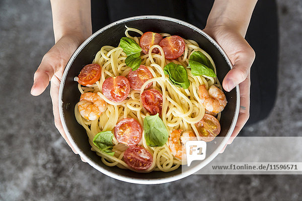 Hände halten Schale mit Spaghetti mit Garnelen  Tomaten und Basilikum