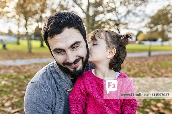 Kleines Mädchen  das seinen glücklichen Vater im Herbstpark küsst.