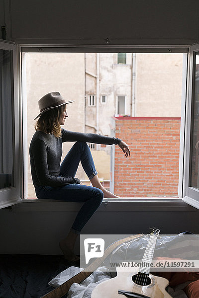 Young woman wearing a hat sitting in window frame