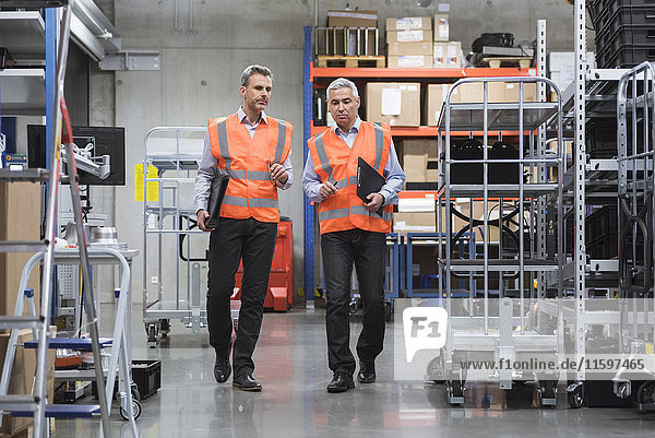 Two colleagues walking in factory hall wearing safety vests