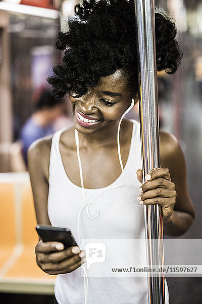 USA  New York City  Manhattan  Porträt einer glücklichen Frau beim Blick auf das Handy in der U-Bahn