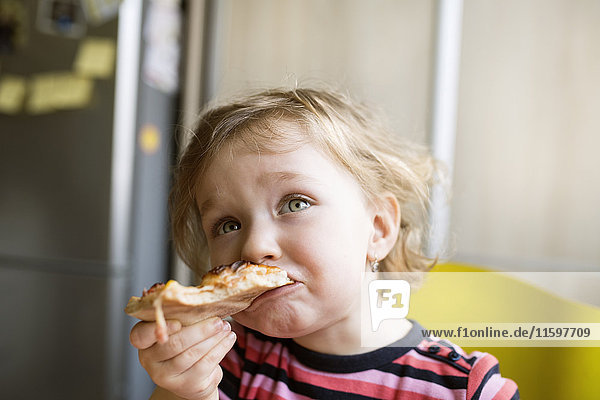 Kleines Mädchen zu Hause isst Pizzastückchen