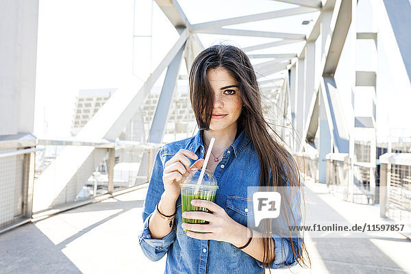 Spanien  Barcelona  Porträt der lächelnden jungen Frau mit Getränk auf einer Brücke