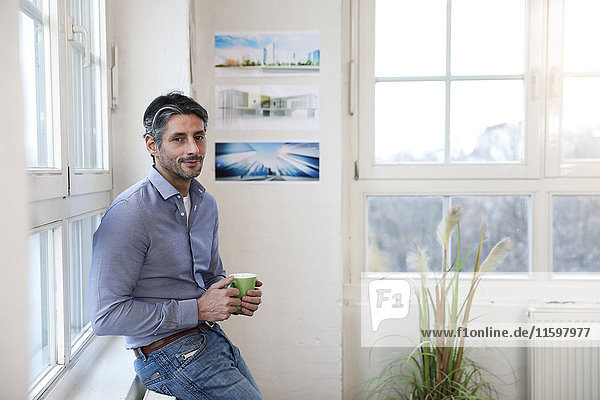 Porträt des lächelnden Mannes mit Tasse Kaffee im Büro