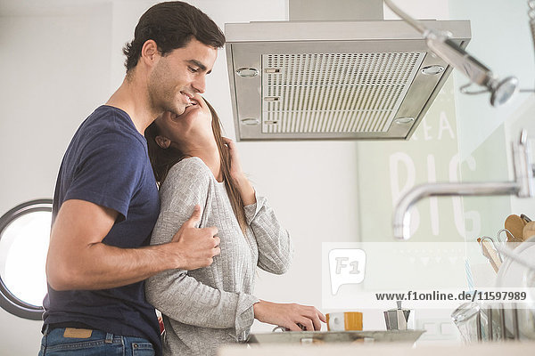 Ein glückliches junges Paar  das in Kaffeetassen in der Küche verliebt ist.