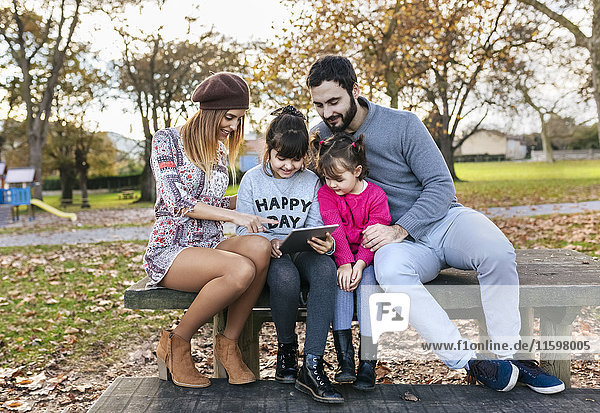 Family sitting on bench in autumnal park looking at tablet