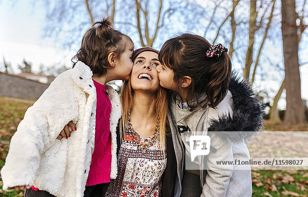 Glückliche Mutter geküsst von ihren kleinen Töchtern