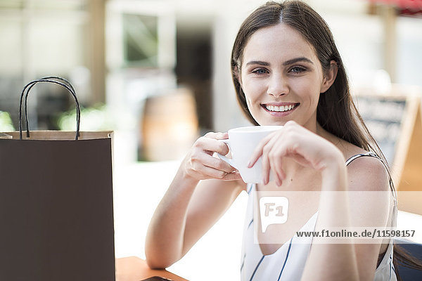 Lächelnde Frau mit Einkaufstasche genießt Kaffee im Cafe