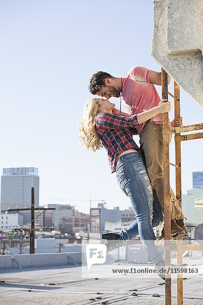 Junges Paar  das sich auf einer Feuerleiter auf dem Dach küsst.