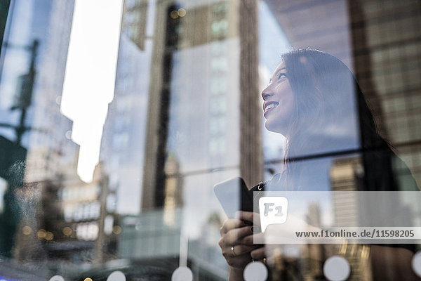 USA  New York City  Manhattan  lächelnde junge Frau hinter Glasscheibe schaut nach oben