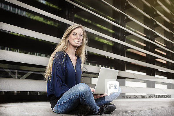 Porträt einer blonden jungen Frau sitzend mit Laptop im Freien