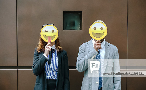 Junger Geschäftsmann und Frau  die Gesichter mit Emoji-Masken bedecken.