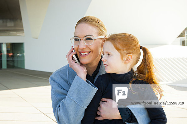 Lächelnde Geschäftsfrau am Telefon umarmt Tochter
