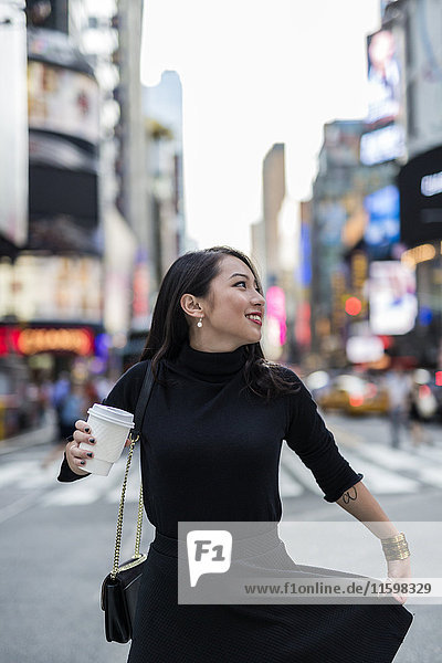 USA  New York City  Manhattan  junge Frau in schwarz gekleidet mit Kaffee  um auf die Straße zu gehen.