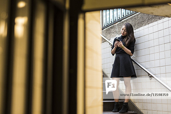 USA  New York City  Manhattan  young woman standing on stairs looking at smartphone