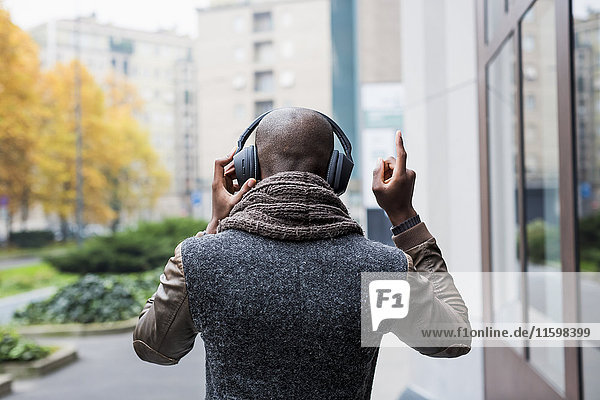 Back view of bald man listening music with headphones