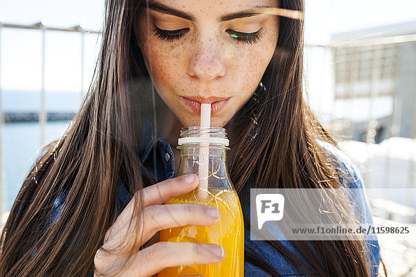 Junge Frau mit Sommersprossen trinkt Orangensaft