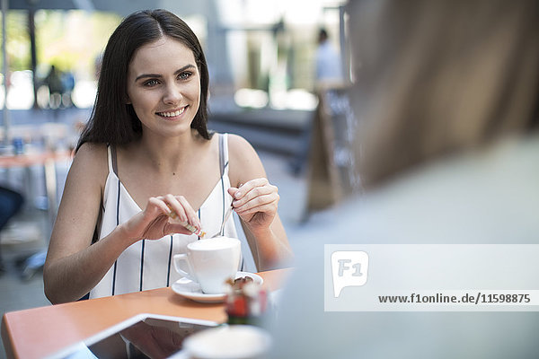 Lächelnde Frau  die einen Freund in einem Café im Freien ansieht.
