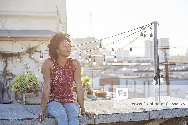 Junge Frau sitzt auf der Dachterrasse und genießt die Sonne.