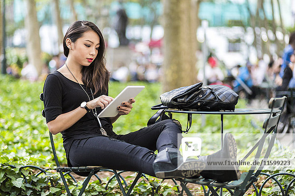 USA  New York  young woman sitting at city park using tablet