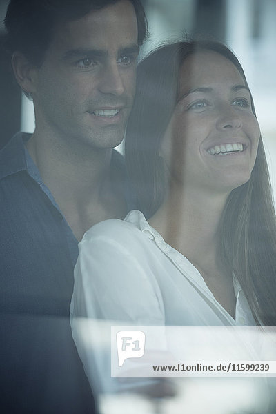 Lächelndes junges Paar schaut aus dem Fenster