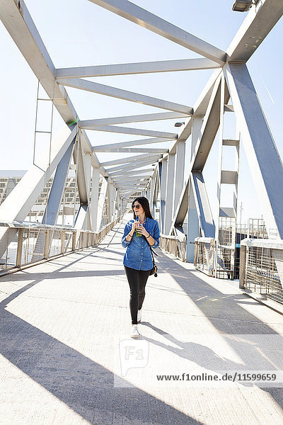 Spanien  Barcelona  lächelnde junge Frau mit Getränk  die auf einer Brücke geht.