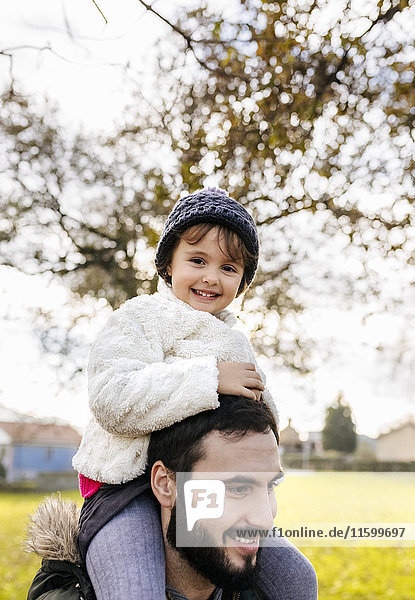 Portrait of happy little girl on shoulders of her father