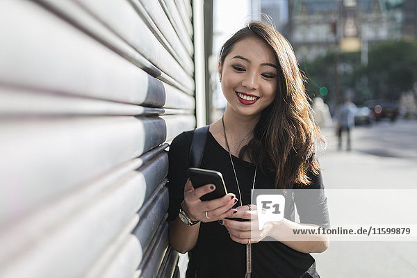 Porträt einer lächelnden jungen Frau beim Blick aufs Handy