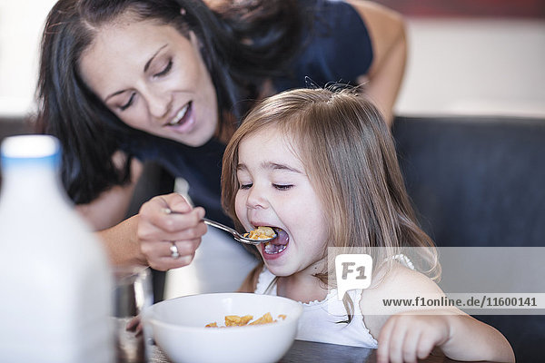 Mutter füttert Tochter Frühstückscerealien am Tisch