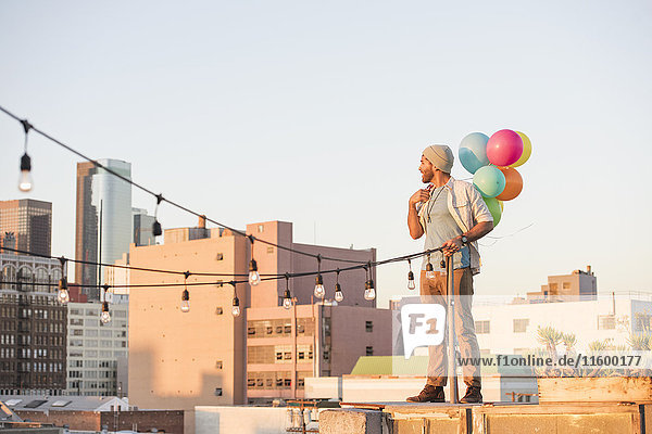 Junger Mann steht auf dem Dach  hält Luftballons