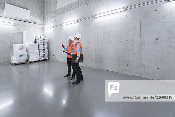 Two colleagues wearing safety vests and hard hats talking in a building