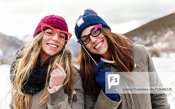 Zwei junge Frauen mit gefälschter Brille haben Spaß in den schneebedeckten Bergen