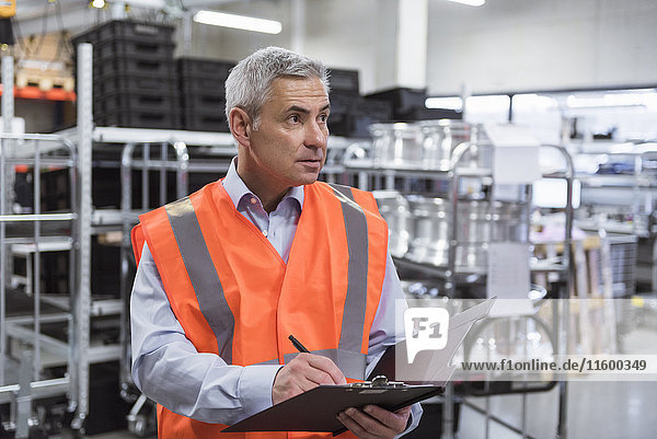 Man in factory hall wearing safety vest holding clipboard