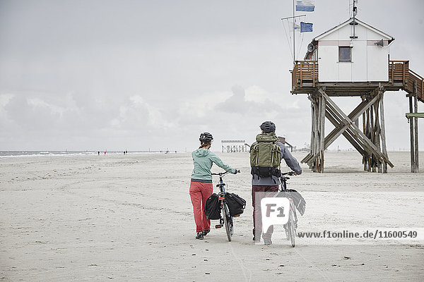 Germany  Schleswig-Holstein  St Peter-Ording  couple pushing bicycles on the beach