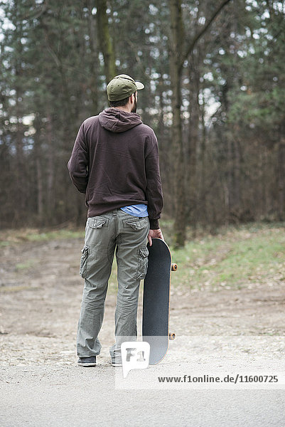 Rückansicht des Mannes im Stehen und Halten des Skateboards