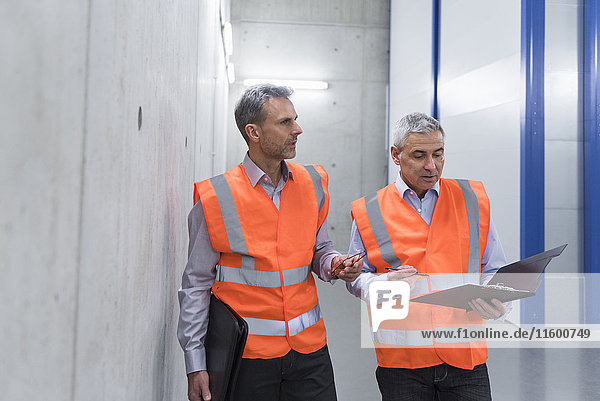 Two colleagues wearing safety vests holding clipboard
