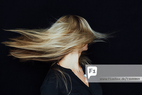 Junge blonde Frau  die ihr Haar vor schwarzem Hintergrund wirft