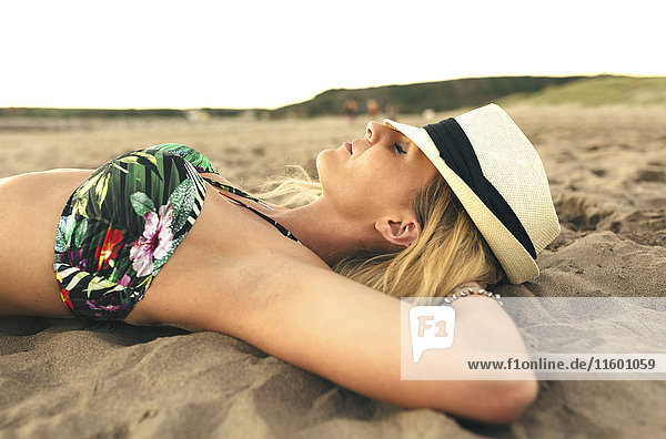Junge Frau mit Hut am Strand liegend mit geschlossenen Augen