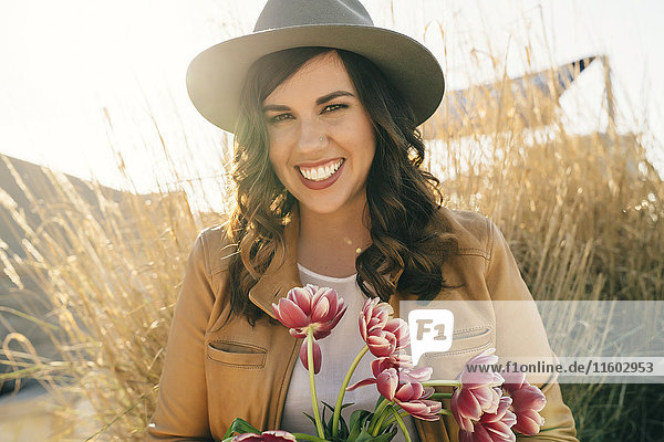 Portrait of smiling Mixed Race woman wearing hat holding flowers