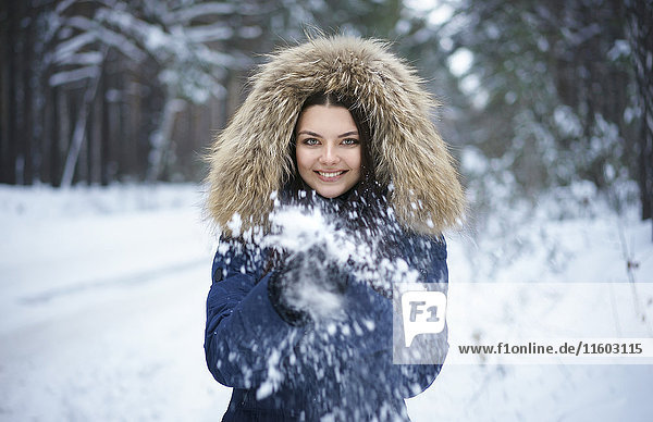 Porträt einer verspielten kaukasischen Frau beim Schneewerfen