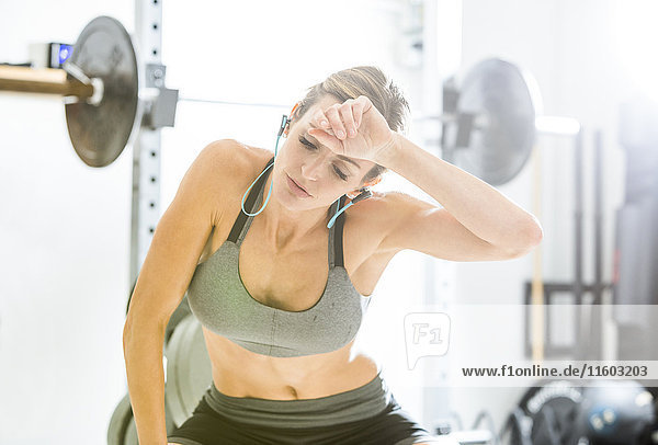 Woman resting in gymnasium wiping sweat from forehead