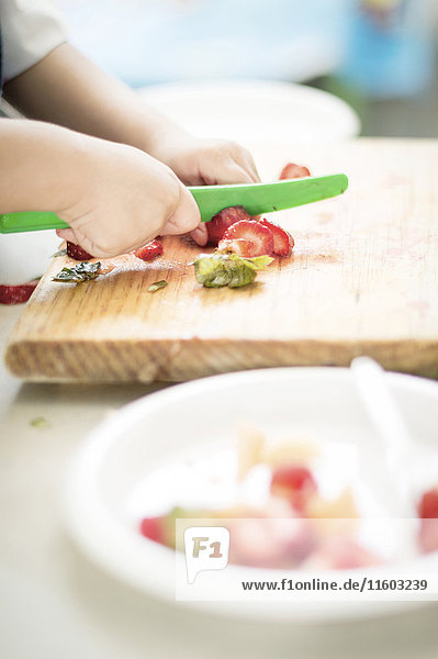 Hands of Hispanic boy cutting strawberry with plastic knife