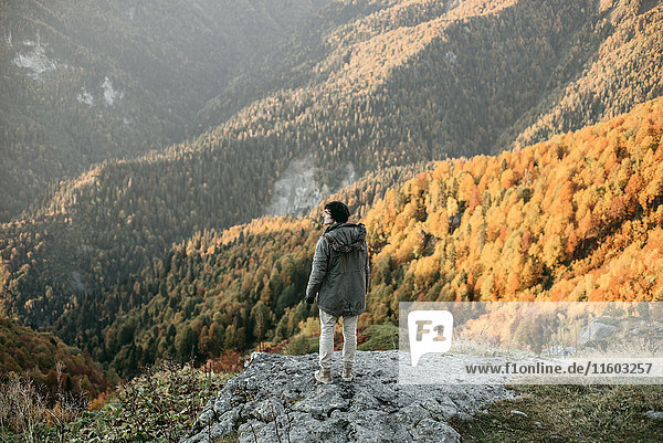 Kaukasischer Mann steht auf einem Bergfelsen und überblickt ein Tal