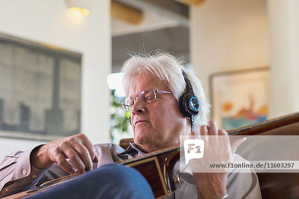 Caucasian man listening to headphones and playing guitar