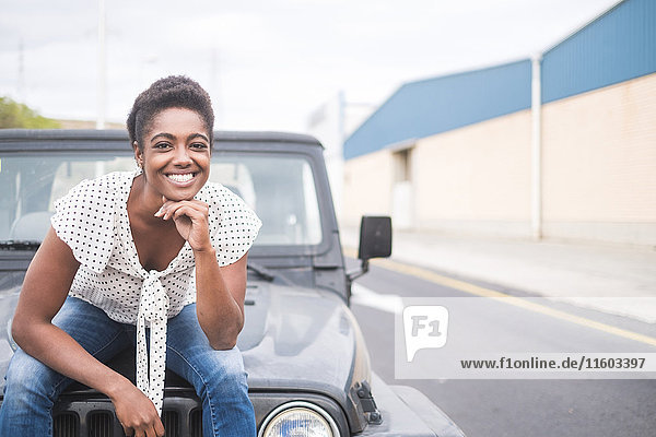 Lächelnde afroamerikanische Frau auf der Motorhaube eines Autos sitzend