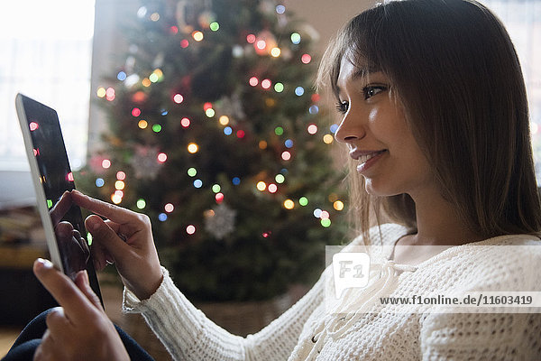 Gemischtrassige Frau benutzt digitale Tafel in der Nähe des Weihnachtsbaums