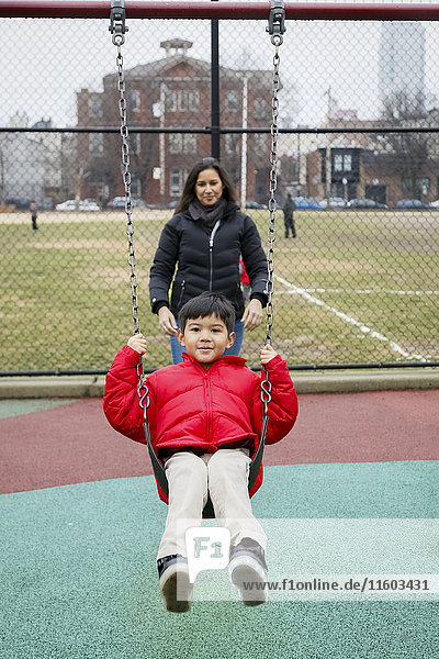 Mutter schiebt ihren Sohn auf dem Spielplatz auf die Schaukel