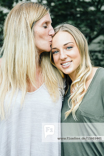 Smiling Caucasian mother kissing forehead of daughter
