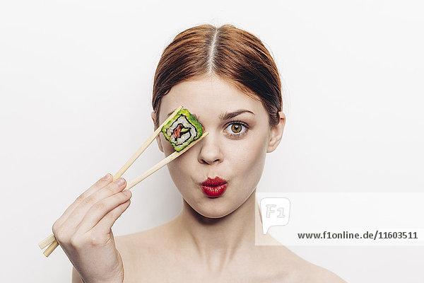 Caucasian woman holding sushi with chopsticks over eye